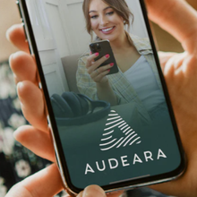 Load image into Gallery viewer, Person holding a phone displaying a woman using a smartphone with Audeara logo.