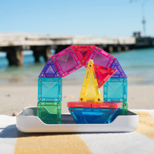Load image into Gallery viewer, A colorful set of transparent magnetic building blocks arranged into an arch and a small boat on a white tray, placed on a beach towel with a blurred ocean and pier background.