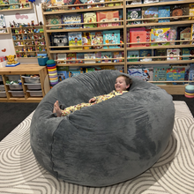 Load image into Gallery viewer, Child sitting inside a large gray bean bag chair in a bookstore.