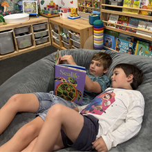 Load image into Gallery viewer, Two children reading books on a bean bag in a classroom setting.