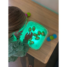 Load image into Gallery viewer, A child's hand reaches into a glowing green light box containing several small decorative eggs, set on a wooden table with other colorful toy pieces nearby.