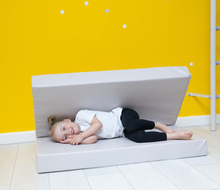 Load image into Gallery viewer, Child lying on a white foam mat against a yellow wall