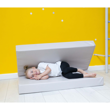 Load image into Gallery viewer, Child lying on a white foam mat against a yellow wall