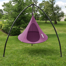 Load image into Gallery viewer, A purple hanging tree swing suspended from a black metal arch frame, set in a grassy backyard with trees in the background.
