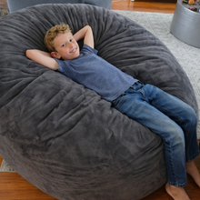 Load image into Gallery viewer, Child sitting inside a large gray bean bag chair in a room with wooden flooring.