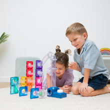 Load image into Gallery viewer, Two children playing with a colorful marble run toy set on a light carpet in a bright room. The set includes translucent blocks, ramps, and wheels in multiple colors, with one child building and the other watching closely.