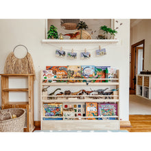 Load image into Gallery viewer, Children's books and toys on a wooden shelf in a room with a white wall and wooden floor.
