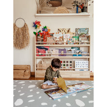 Load image into Gallery viewer, Child reading a book on a patterned rug in a room with educational toys and books.