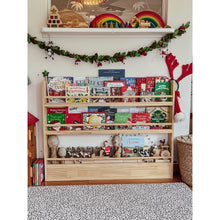 Load image into Gallery viewer, Bookshelf filled with Christmas-themed books and decorations in a room with festive decor.