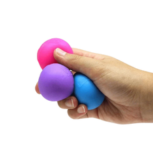 Load image into Gallery viewer, A hand squeezing three small round stress balls in pink, purple, and blue against a plain white background.