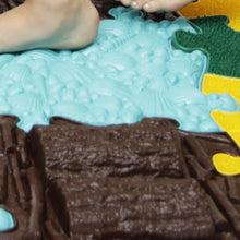 Load image into Gallery viewer, Close-up of a chocolate cake with blue icing shaped like water and a yellow flower on a green base.
