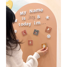 Load image into Gallery viewer, Person interacting with a wall display featuring 'My Name is izzy &amp; today im' text and various small cards.
