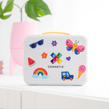 Load image into Gallery viewer, A white Connetix lunch box with a yellow handle, decorated with colorful cartoon stickers including a butterfly, rainbow, sunglasses, watermelon, ice cream cone, and flowers, set on a white shelf with a pink planter in the background.
