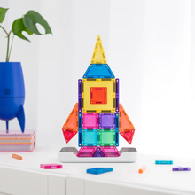 Load image into Gallery viewer, A colorful magnetic tile rocket toy built on a white surface, with loose tiles scattered around and a blue plant pot in the background.

