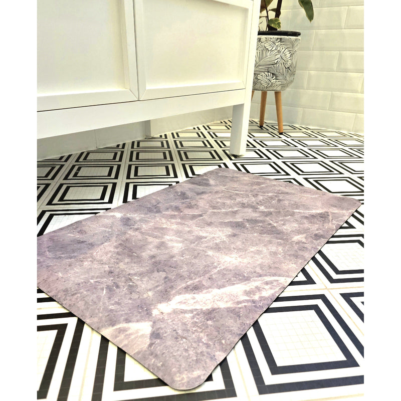 A gray diatomite bath mat with a non-slip surface is laid out on a tiled bathroom floor, showing its quick-drying feature after being stepped on.
