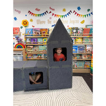 Load image into Gallery viewer, Child playing inside a gray block structure in a classroom setting with books and decorations on the wall.
