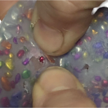 Load image into Gallery viewer, Close-up of a hand holding a small red gemstone over a colorful glittery surface.
