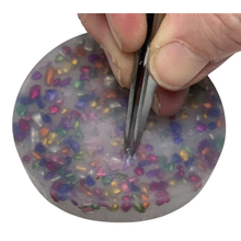 Load image into Gallery viewer, Hand using tweezers to manipulate a colorful, gel-like substance with embedded small beads.
