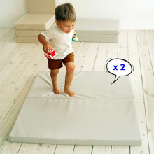 Load image into Gallery viewer, Child standing on a large mat with two smaller mats stacked behind, in a minimalistic room.

