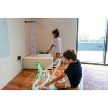Load image into Gallery viewer, Two children playing with toys in a modern room with large windows.
