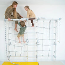Load image into Gallery viewer, Children playing on a climbing net with a woman supervising, against a white wall.
