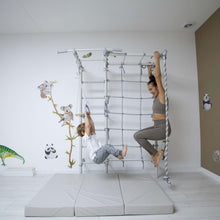 Load image into Gallery viewer, Two children playing on a climbing frame in a room with white walls and a brown door.
