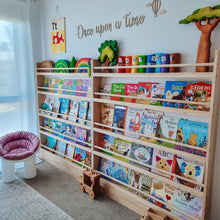Load image into Gallery viewer, Children's bookshelf with colorful books in a room with a chair and decorative elements.
