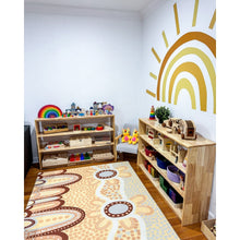 Load image into Gallery viewer, Children&#39;s playroom with wooden shelves filled with toys, a colorful rug on the floor, and a rainbow wall decal.
