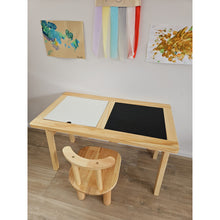 Load image into Gallery viewer, Wooden children's table with white and black surface and matching chair, against a wall with colorful decorations.
