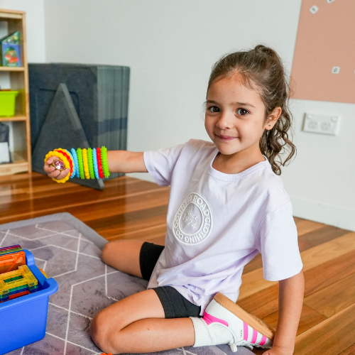 Child playing with colorful toy in a room with books and a rug.