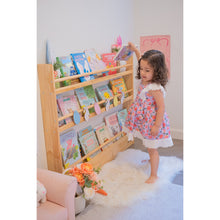 Load image into Gallery viewer, Child standing next to a wooden bookshelf filled with books in a room.
